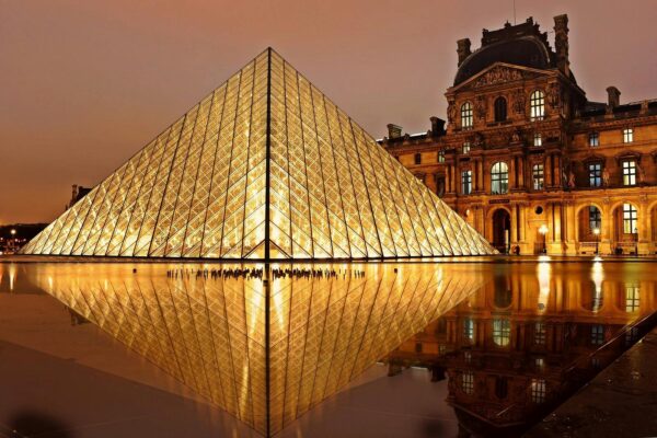 Stunning nighttime view of the illuminated Louvre Pyramid and reflection in Paris, France.