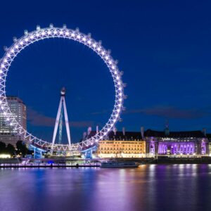 The illuminated London Eye reflects over the River Thames at night, showcasing vibrant city lights.