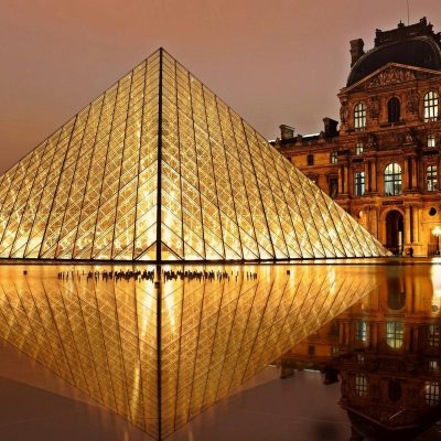 Stunning nighttime view of the illuminated Louvre Pyramid and reflection in Paris, France.